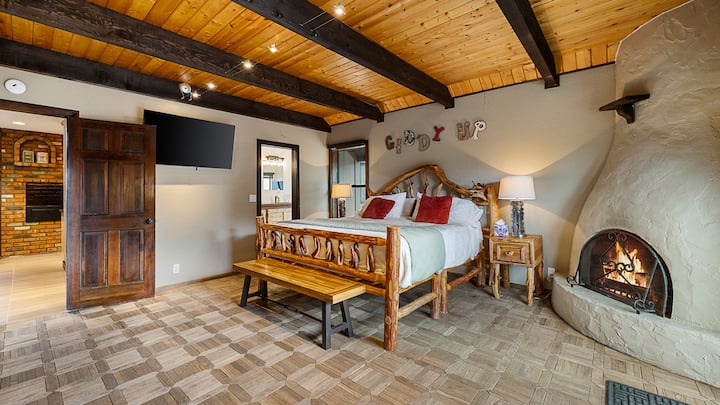 חדר שינה קינג-סייז בסגנון כפרי עם מיטת עץ, קמין מאבן וחדר רחצה צמוד.