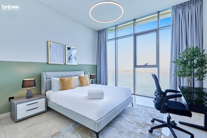 Priestranná spálňa s manželskou posteľou a oknami od podlahy až po strop s panoramatickým výhľadom na more, v spojení s elegantným pracovným stolom a stoličkou — dokonalá rovnováha medzi pohodlím a produktivitou.