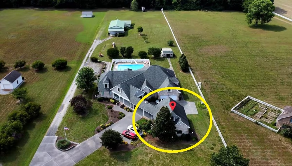 An aerial view depicts the guest suite, nestled among lush greenery, with a spacious swimming pool nearby. The main house, along with various outdoor amenities, is visible, showcasing well-maintained landscaping and open fields surrounding the property.