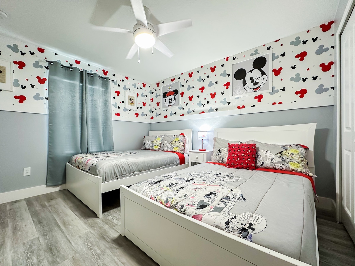 ¡Sumérgete en la magia de Disney con este fantástico retiro de Mickey y sus amigos! Dos camas individuales vestidas con ropa de cama clásica con estampado de dibujos animados se encuentran bajo un ventilador de techo, rodeadas de un divertido papel pintado con siluetas de Mickey.                                             