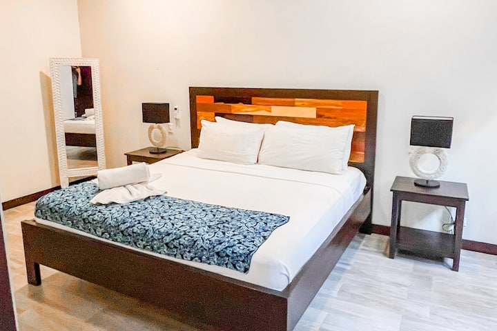 La photo montre une chambre confortable et accueillante avec un lit confortable, des tables de nuit avec des lampes et un miroir pleine longueur. La chambre a une sensation légère et aérée avec des couleurs neutres et une lumière naturelle.