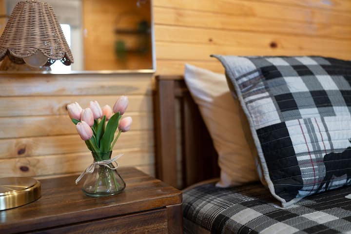 A little rustic, a little chic, and totally cozy! This cute bedside setup has all the right touches—a charming wicker lamp, cozy plaid bedding, and a pop of pink tulips—because even a cabin needs a little flair!
