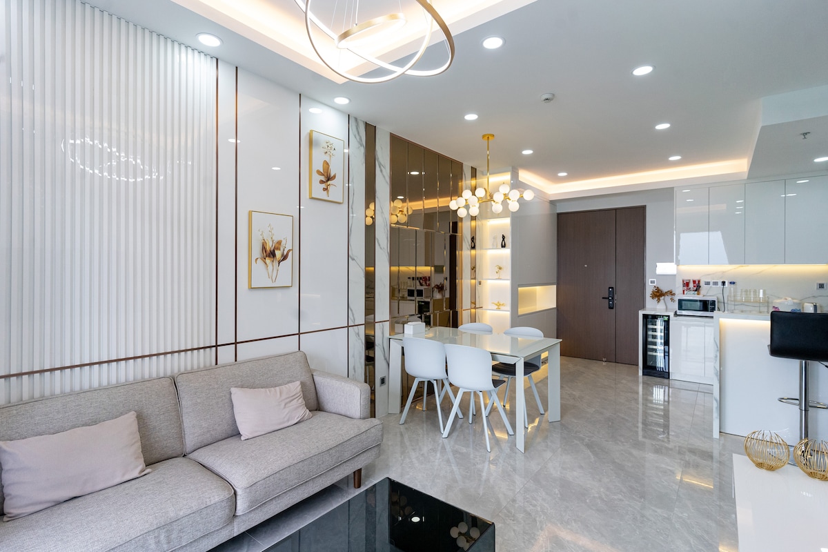 The living area features a light-colored sofa with soft cushions, complemented by a minimalist dining table surrounded by white chairs. Stylish lighting fixtures illuminate the space, while sleek cabinetry adds a modern touch. The open layout enhances the feeling of spaciousness.