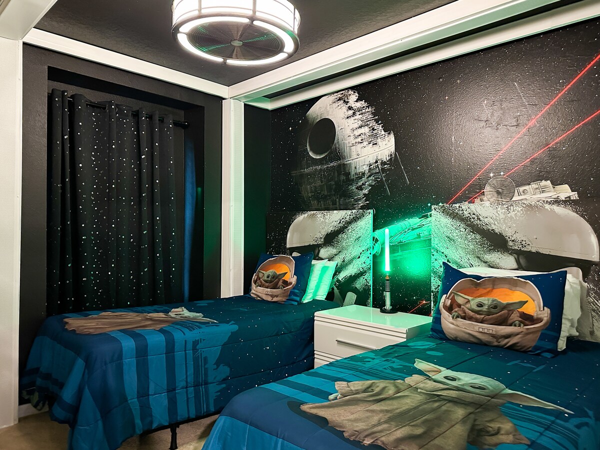 Ჩაწერეთ გალაქტიკათშორისი სამალავი: ვარსკვლავებით მოჭედილი შავი კედლები და ჭერის კონვერტირებული ტყუპი ბეიბი იოდას თემატიკის საწოლები, რომლებიც თეთრ ტუმბოზე დგას. Ნეონის ლურჯი შუქდიოდური მორთვა, ორმაგი სანათებიანი ნათურები, უშუქო ფარდები და ქარიშხლის მოხატულობა.                        