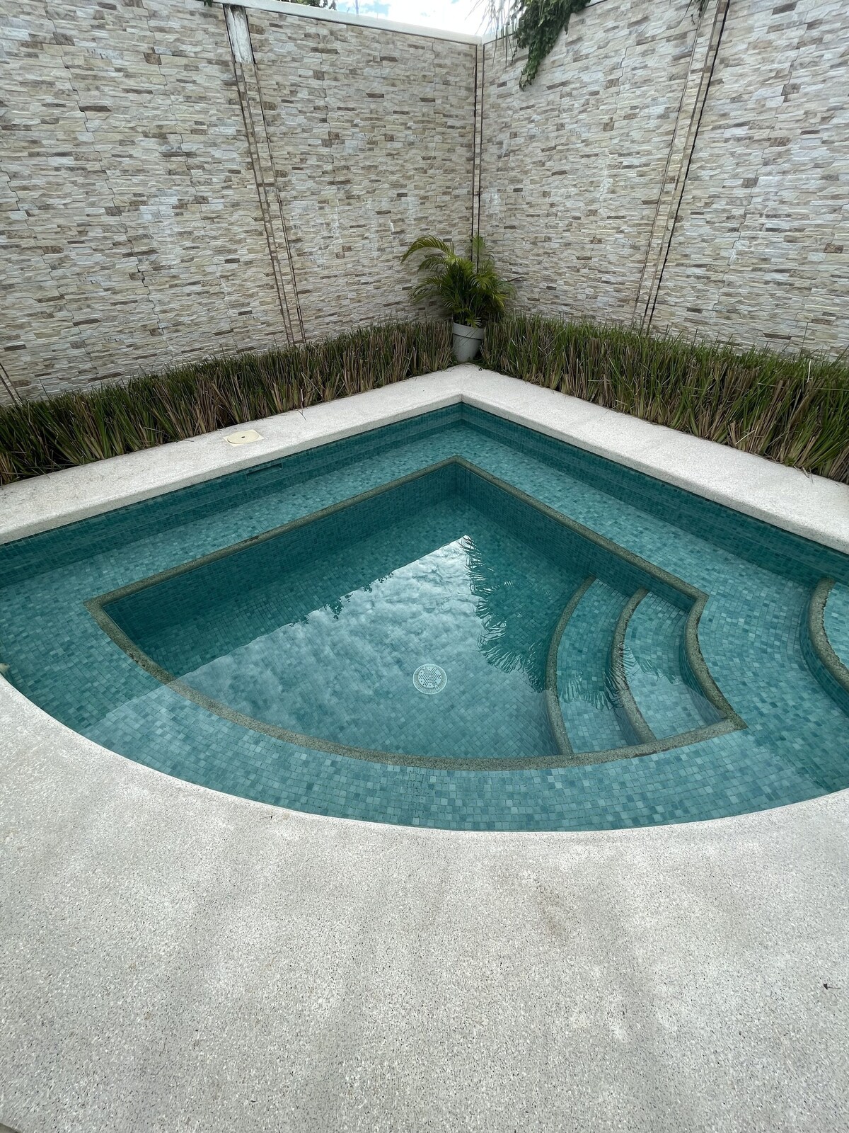 A private pool is set within a rectangular terrace, featuring clear water and smooth stone surfaces. Textured stone walls create a serene backdrop, complemented by greenery along the edge, enhancing the feeling of seclusion.