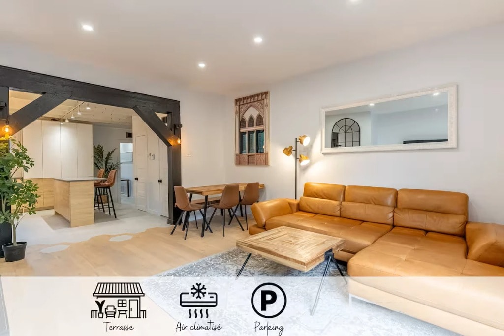 A bright and inviting living space features a comfortable brown leather sectional sofa paired with a stylish wooden coffee table. Natural light filters through large windows, highlighting the modern decor. A potted plant adds a touch of greenery, creating a warm atmosphere in the open layout.