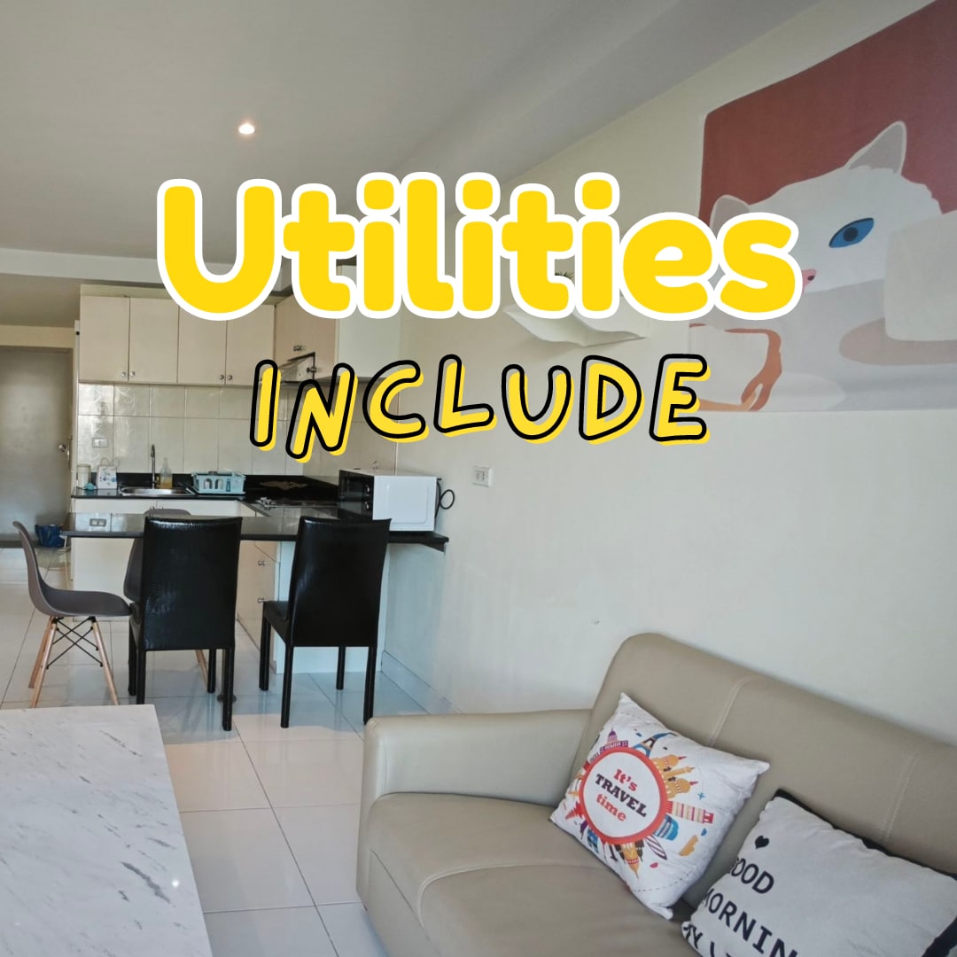 A modern kitchen area features a marble dining table and black chairs against a backdrop of light cabinetry. Kitchen appliances, including a microwave and kettle, are visible. A comfortable sofa with cushions displays a welcoming message, contributing to the cozy ambiance of the living space.