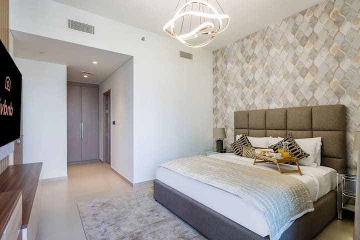 Spálňa s čalúneným čelom, vzorovanou stenou a mäkkým osvetlením.