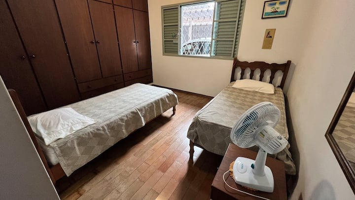 quarto 4 com duas camas de solteiro, um ventilador e um guarda roupa.