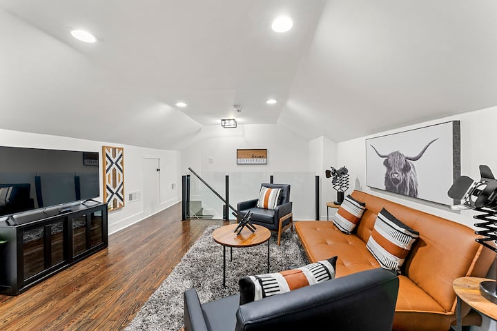 Modern loft-style living area featuring a sleek leather sofa, cozy armchairs, and a large TV for entertainment. The space is adorned with contemporary art and warm lighting, making it perfect for relaxation or gathering with family and friends.