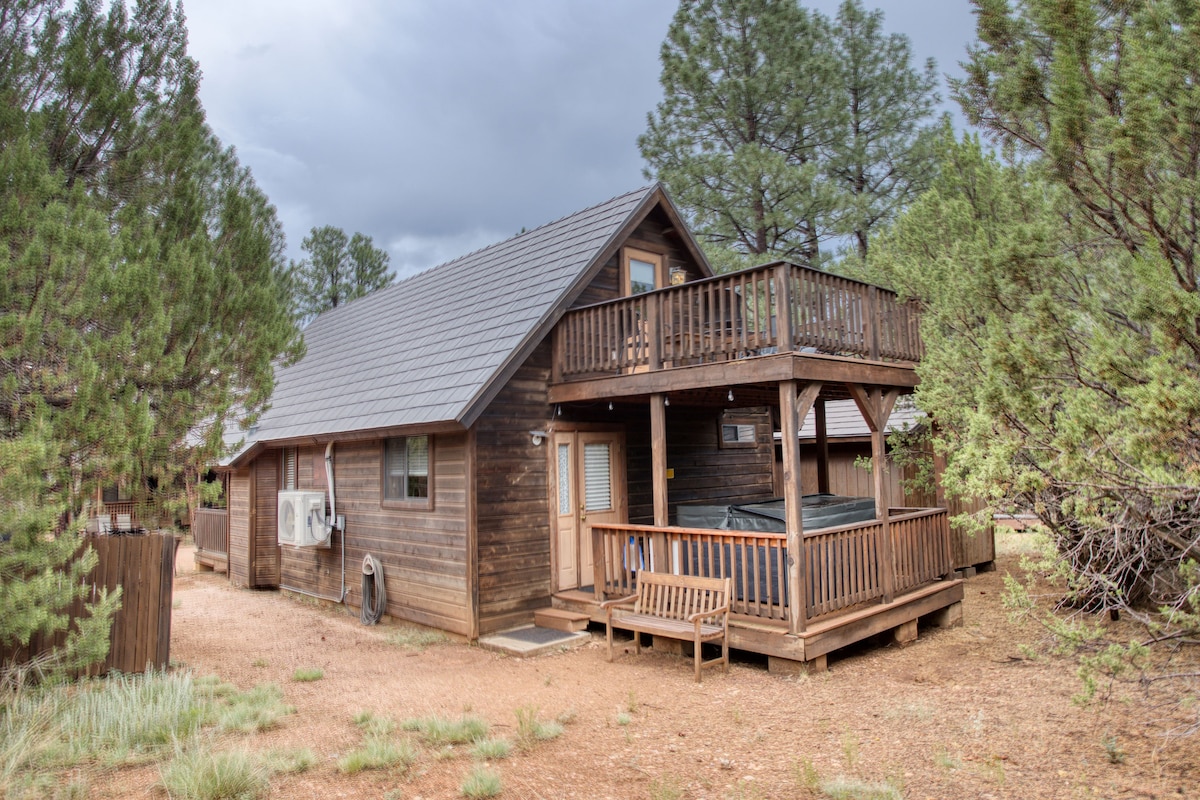 The exterior of the cabin showcases a two-story structure nestled among tall pine trees. A private deck with a new hot tub is visible, accompanied by outdoor seating. The facade features natural wooden siding, and a cozy porch area is included.