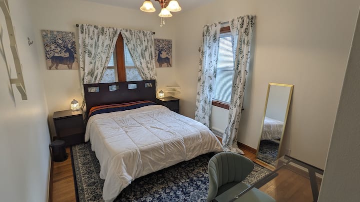 เตียงควีนไซส์พร้อมโต๊ะข้างเตียง 2 ตัวพร้อมลิ้นชัก + ชั้นวางของแต่ละอันที่แขวนเสื้อผ้าติดผนัง 1 อันตู้เสื้อผ้าพร้อมชั้นวางของและโต๊ะทำงาน + เก้าอี้ หน้าต่างด้านหลังเตียงมองเข้าไปในระเบียงด้านหน้าที่ล้อมรอบ หน้าต่างด้านข้างมองเข้าไปในลานด้านข้าง