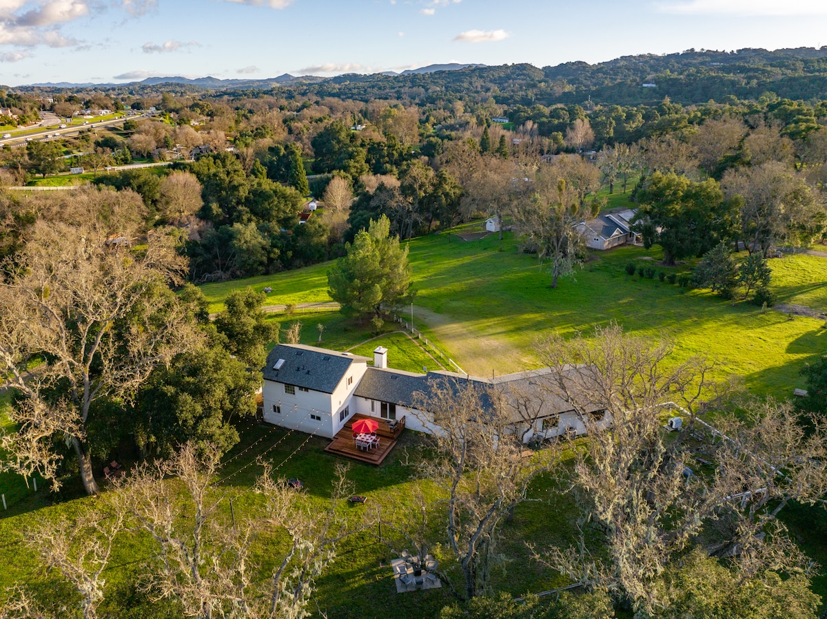 An aerial view showcases the spacious 4.2-acre property, featuring a well-maintained home surrounded by greenery. Scenic hills and trees provide a tranquil backdrop, while the nearby freeway is visible in the distance, reflecting the home's accessible yet private location.