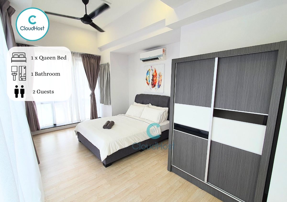 A modern studio suite is presented with a spacious queen bed, framed by large windows allowing natural light. A wardrobe with a sleek design stands nearby, and a colorful artwork adds a pop of vibrancy to the neutral walls. Amenities for comfort are also visibly arranged.