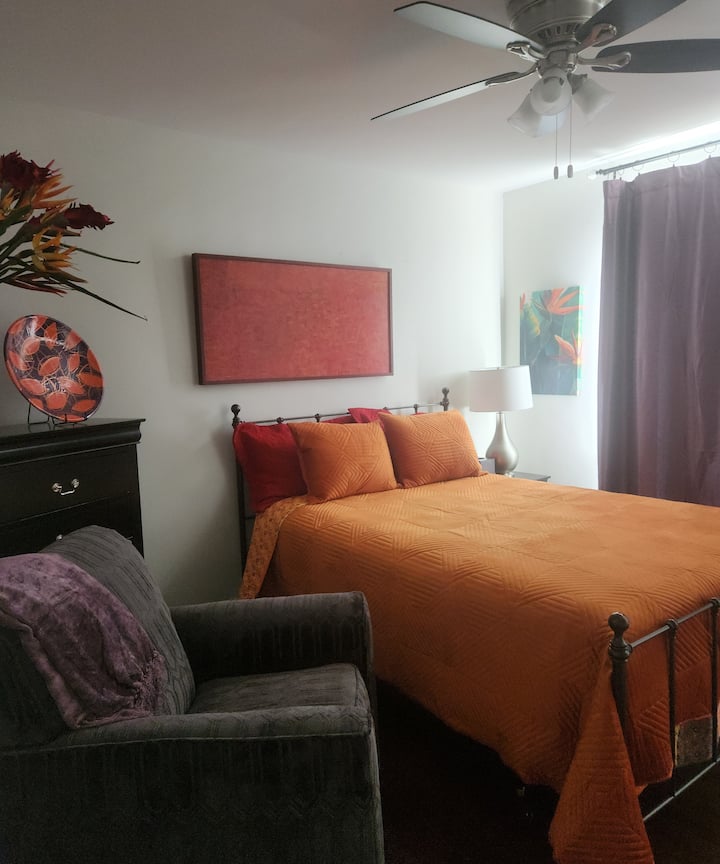 Chumba hiki kilichopambwa kwa rangi ya chungwa na zambarau, kilichopambwa kwa rangi ya chungwa na zambarau, kina kitanda cha ukubwa wa malkia kilicho na godoro linaloweza kurekebishwa, plagi ya USB na televisheni ya inchi 50.