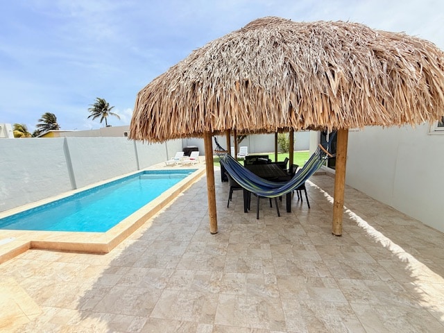 A private gazebo with a thatched roof provides shaded seating around a large table. Adjacent is a crystal-clear saltwater pool, with lounge chairs set for relaxation. The surrounding tiled area contributes to a spacious outdoor environment, ideal for leisure activities.