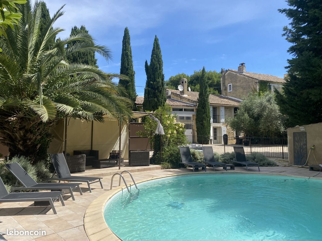 A private round swimming pool, measuring 9 meters, is surrounded by sun loungers and leafy palm trees. The tranquil outdoor space features a shaded area and a stone patio, with a charming stone building visible in the background, providing a serene atmosphere.