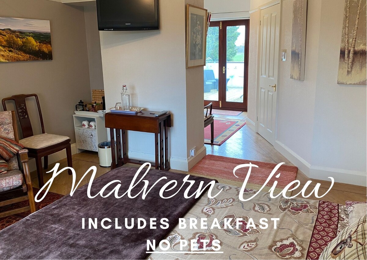 A well-appointed room features a cozy seating area with two chairs and a small table, alongside a flat-screen TV mounted on the wall. There are wood and carpeted floors, and the entrance to a private terrace can be seen, providing easy access to outdoor space.