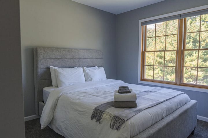 Მეორე სტუმრის საძინებელი მთავარ სართულზე, დედოფლის ზომის მატრასითა და მასიური უკანა ეზოს ხედით.