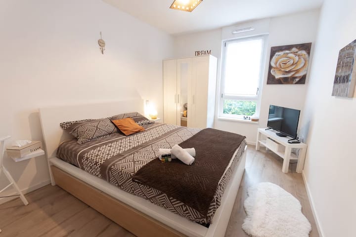 Habitación luminosa y acogedora con una cama grande y acogedora, TV y almacenamiento, ideal para noches relajantes.