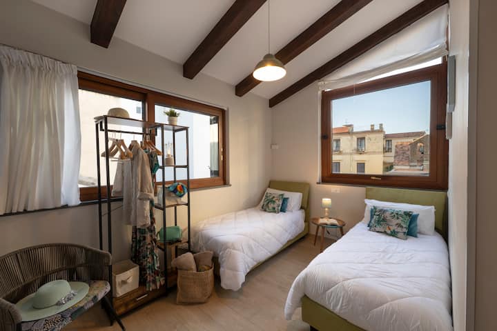 Segundo dormitorio con dos camas de matrimonio, convertible si es necesario en una cama doble. Los grandes ventanales ofrecen una vista de las azoteas e iglesias circundantes, con acceso directo a la terraza privada para momentos de relajación al aire libre.