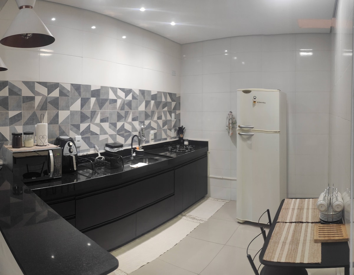 A modern kitchen is visible, featuring sleek black cabinetry and a patterned backsplash. Essential appliances include a refrigerator, microwave, and stove. A small dining table with two chairs is present, complemented by tableware neatly arranged on it. Ample counter space offers convenience for meal preparation.