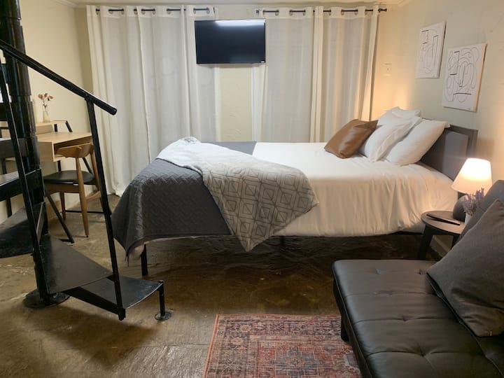 ห้องสวีทควีนไซส์ชั้นล่างพร้อมเตียงควีนไซส์ที่อบอุ่น ผ้าปูที่นอนนุ่ม การตกแต่งที่สงบ สมาร์ททีวี โต๊ะทำงาน และห้องน้ำส่วนตัว เหมาะสำหรับผู้เข้าพักที่ต้องการพื้นที่ ต้องใช้บันไดวนเพื่อเข้าชั้นล่าง