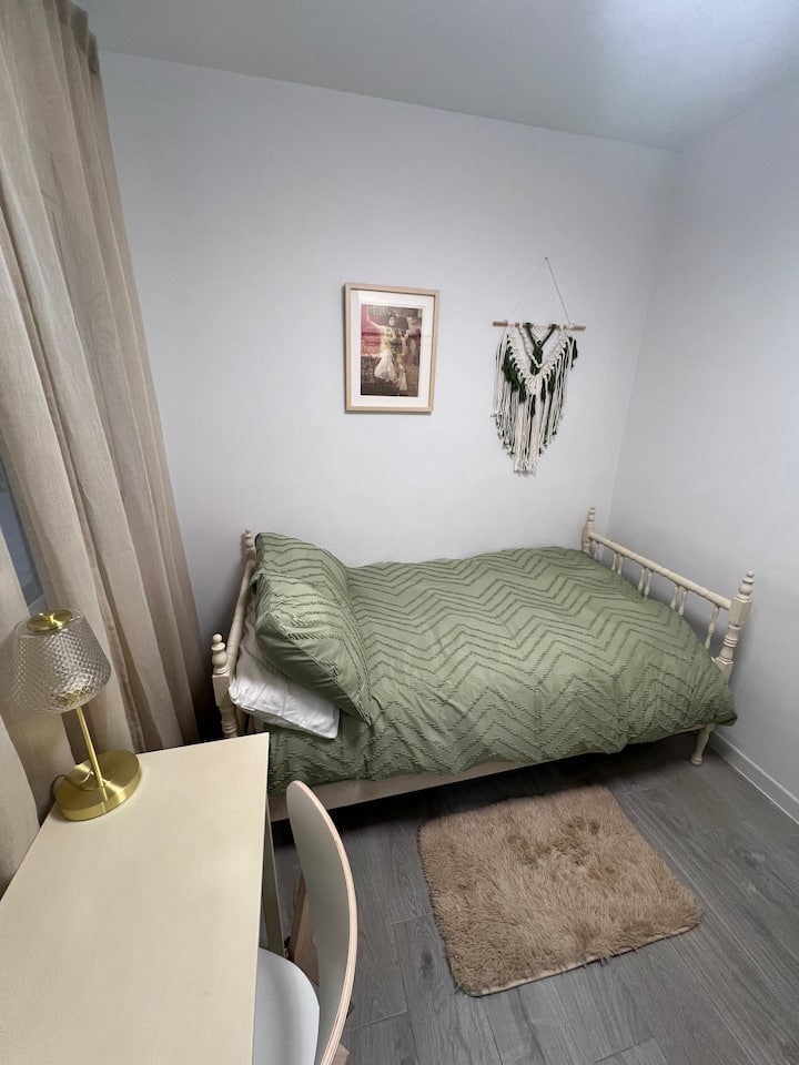 Acogedor dormitorio con cama individual, armario con cajones y mesa de escritorio. Muebles reciclados en color marfil y textiles en tonos verde hoja aportan frescura y naturalidad. Una lámina costumbrista y decoración en macramé completa ambiente.