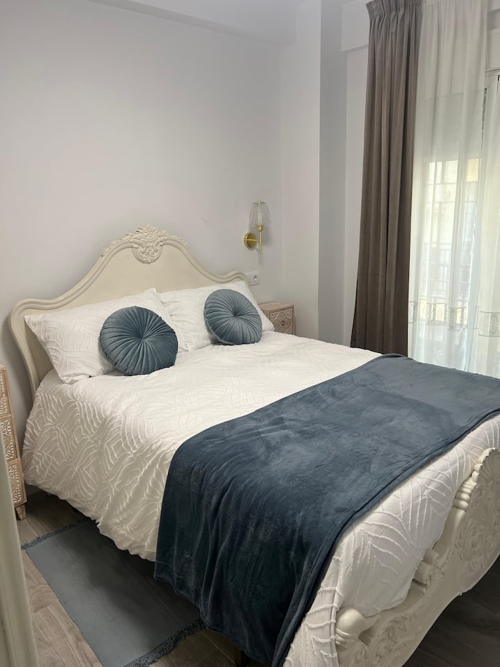 Estilo y sostenibilidad se combinan en el dormitorio principal, con muebles reciclados y pintados en un fresco color blanco, incluyendo una cama doble y un amplio ropero. La cómoda azul celeste añade un toque de color y personalidad al ambiente.