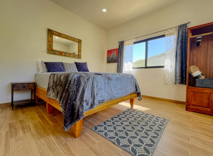 Espace chambre au rez-de-chaussée avec deux grandes fenêtres avec une charmante vue sur les collines arrière. Accédez à cette chambre depuis le salon. Une salle de bain complète se trouve à quelques pas de la porte de la chambre.