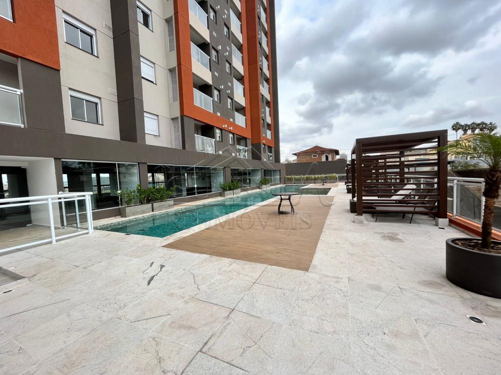 A swimming pool area is presented outside a modern building. Sun loungers are positioned beside the pool, surrounded by a wooden deck. Lush greenery is visible nearby, contributing to a relaxed outdoor ambiance, while the building's contemporary architecture provides a striking backdrop.