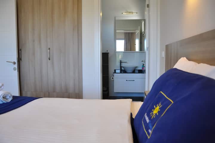 « Chambre principale : lit double de 160 × 200, rideaux opaques et climatisation. Salle de bain attenante avec douche à côté de l'armoire coulissante. Accès au balcon face à l'avant de la pièce, vue partielle sur la mer/forêt. Un lit pour bébé peut être ajouté si vous le souhaitez. »