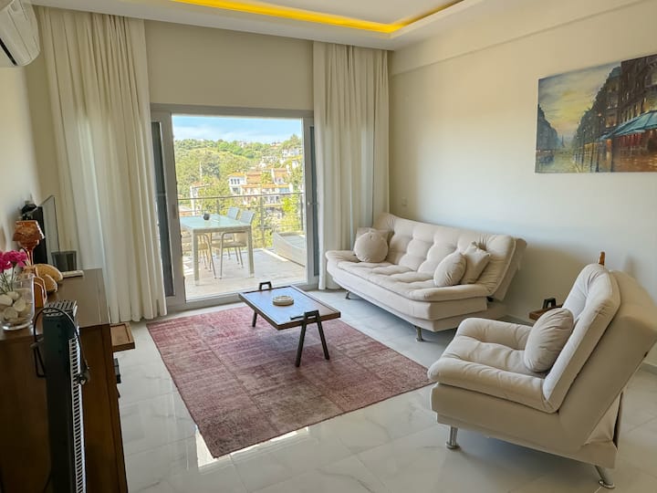 Salon lumineux à haut plafond; climatisation, rideaux occultants et télévision intelligente + IPTV. L'espace ouvert communique avec la cuisine, mène à un balcon/terrasse spacieux; il y a ici une table pour 6 personnes et une vue partielle sur la forêt de mer. Possibilité de couchage supplémentaire avec canapé-lit + lit pliant.