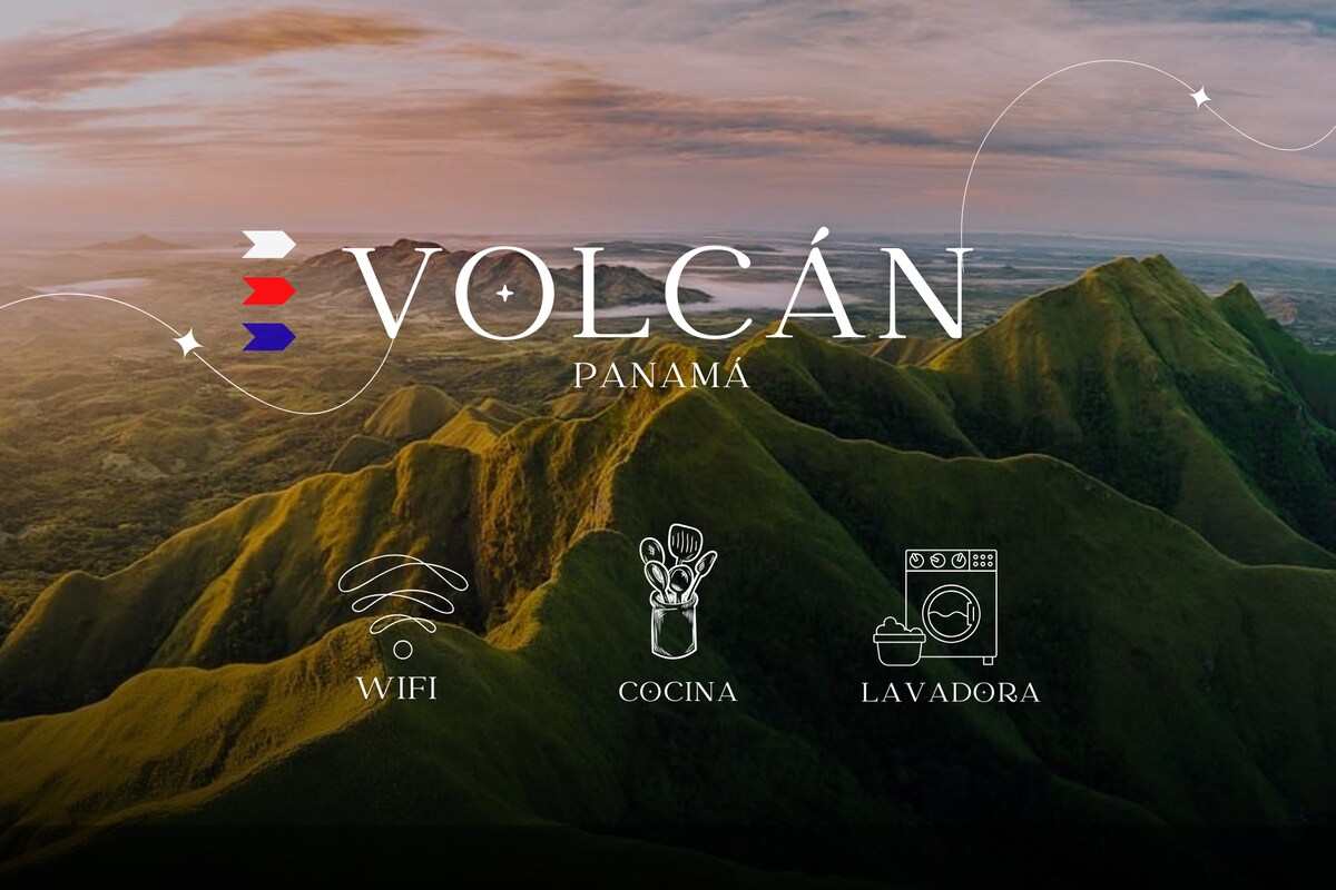 A scenic view of lush green mountains is captured under soft morning light. The name 'Volcán' is prominently displayed alongside icons representing WiFi, kitchen facilities, and laundry appliances, indicating available amenities for guests.