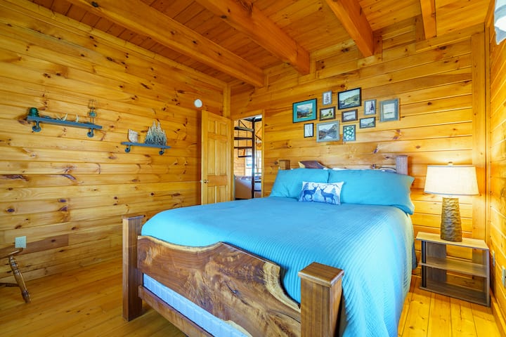 חדר בקתה נעים עם מיטת קווין סייז עם שני חלונות גדולים לאור נהדר ונוף ליער שמסביב.