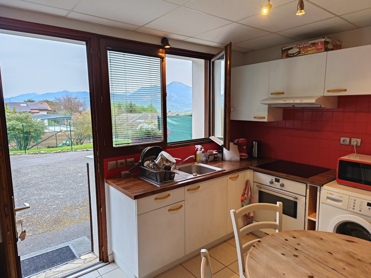 A well-equipped kitchen is presented with modern appliances, including a stove and microwave. Natural light enters through large windows, offering views of the surrounding mountains. A round table with chairs is situated nearby, enhancing the functional space for dining or preparation.
