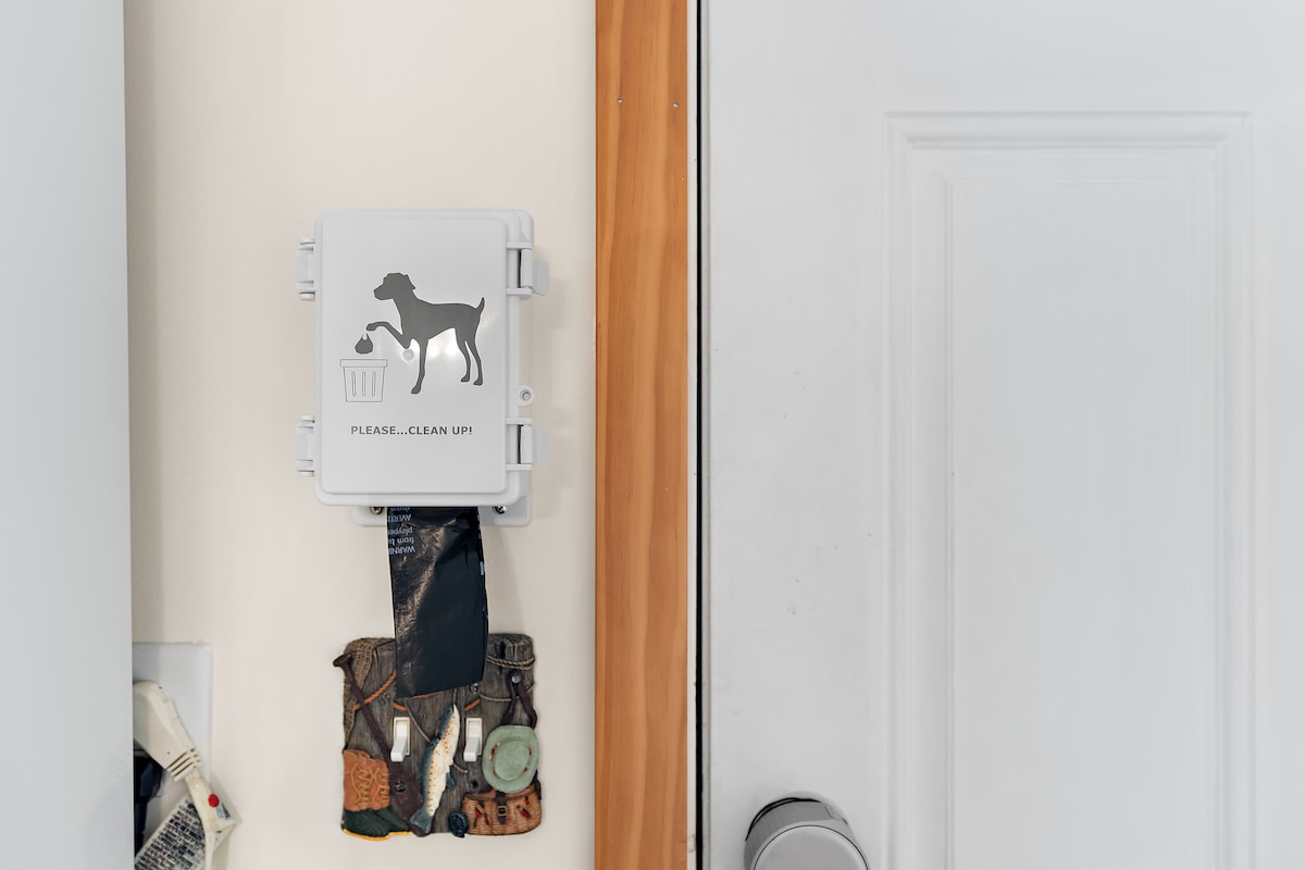 A dog waste disposal station is mounted near the entrance door, featuring a silhouette of a dog and a trash bin. Below, a collection of dog waste bags is attached, ensuring convenience for guests with pets.
