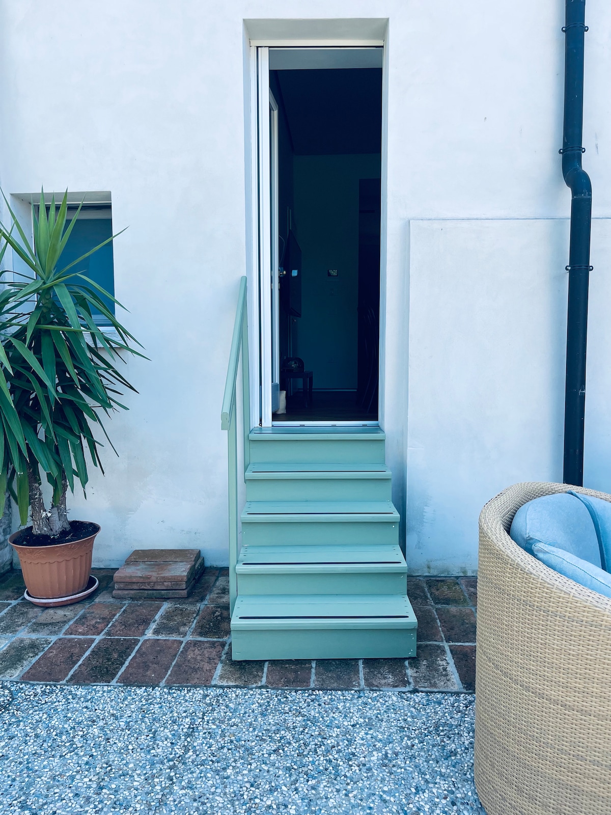 A set of pale green stairs leads to an entrance, framed by a potted palm on the left. The stairs are situated against a light-colored wall, providing a welcoming access point to the property.