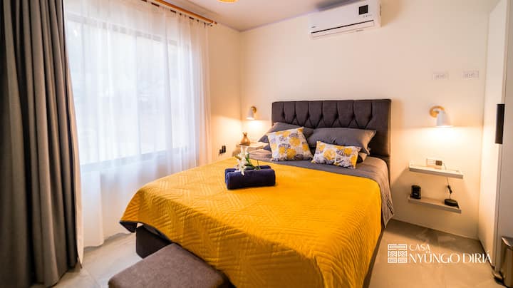 Relájate en nuestro elegante dormitorio con una cómoda cama tamaño queen con ropa de cama de lujo, que ofrece un ambiente tranquilo para un sueño rejuvenecedor.