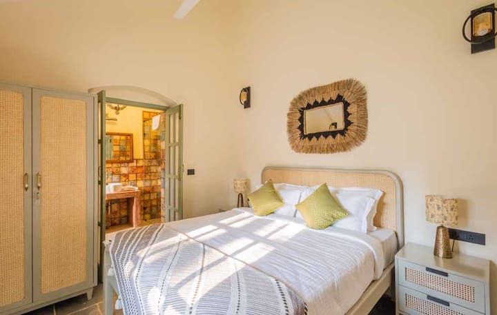 A queen bedroom that combines traditional cane furniture with modern wall art, comes with an en-suite bathroom that offers luxurious amenities and a smart TV for entertainment.