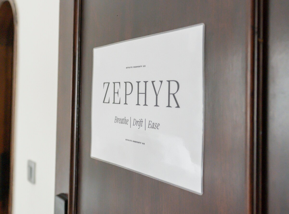 A wooden door is prominently displayed, featuring a sign that reads 'ZEPHYR' with the words 'Breathe | Drift | Ease' beneath it. The sign is neatly arranged, suggesting a calm and inviting space behind the door.