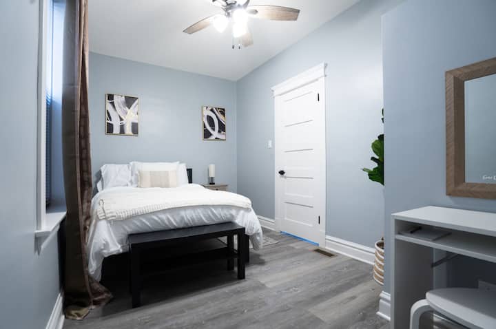 Entdecke ein ruhiges Schlafzimmer mit einem komfortablen Queensize-Bett und abdunkelnden Farbtönen, die einen erholsamen Schlaf gewährleisten. Ein vielseitiger Schreibtisch bietet den perfekten Raum für Produktivität oder kann leicht in einen stilvollen Schminktisch verwandelt werden.