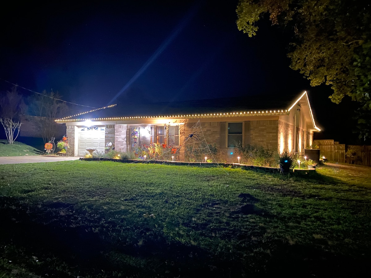The exterior of the home is illuminated by warm lights along the roofline, creating a welcoming ambiance at night. A well-manicured lawn is visible in front, with soft lighting highlighting the landscaping elements.