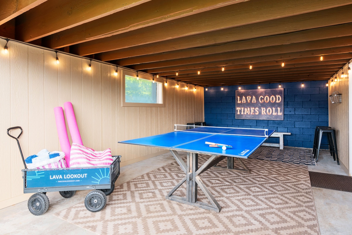 An entertaining game room is equipped with a ping pong table and playful décor. A wagon filled with pool noodles and towels rests nearby. The space features soft lighting and a sign reading 'LAVA GOOD TIMES ROLL,' contributing to a relaxed atmosphere.