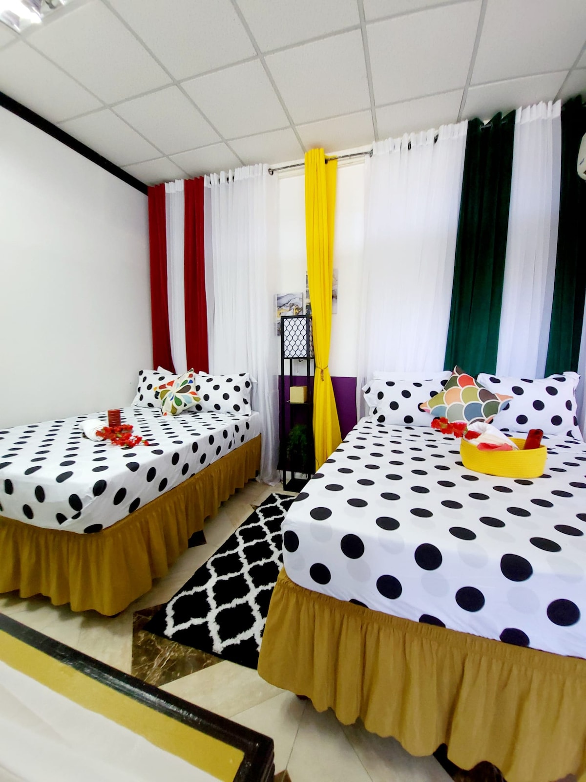 This stylish space features two comfortable beds adorned with playful polka dot linens, complemented by a burst of colorful decor. Enjoy the lively mix of red, green, yellow, and white curtains that create a cheerful atmosphere, ideal for relaxation.