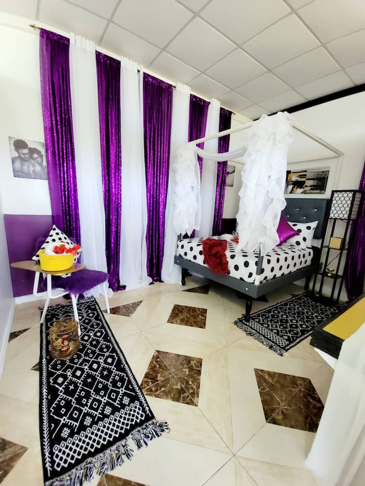 Relax and unwind in our chic and vibrant bedroom, featuring eye-catching purple sequin curtains and stylish decor. The room offers a cozy seating area with a plush chair and a small table, perfect for enjoying a snack or reading a book.