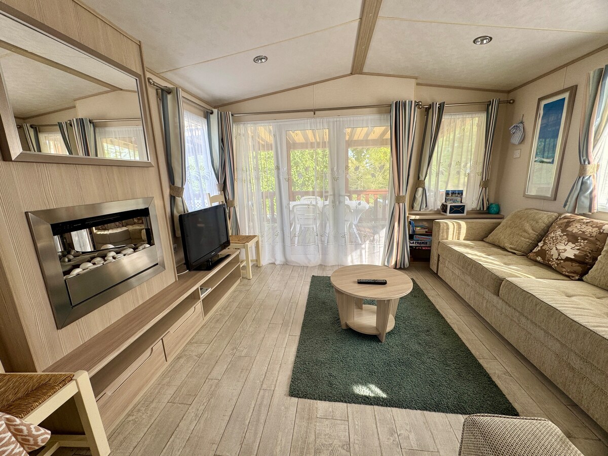 Amplio salón con un ambiente acogedor, equipado con una "chimenea" eléctrica, TV, zona de lectura y juegos de mesa, con vistas a la terraza cubierta con vistas al lago.