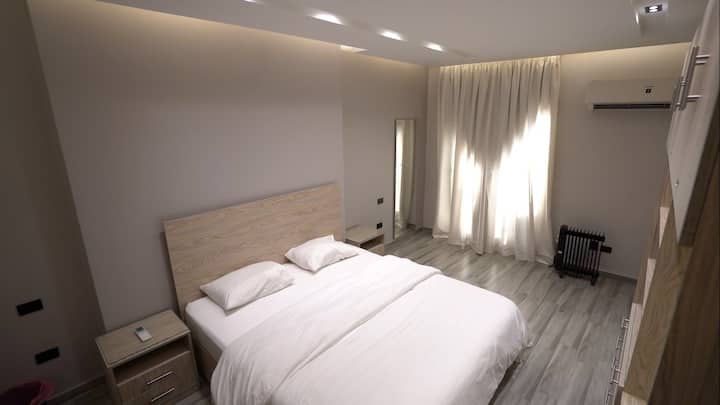 快適なダブルベッド、落ち着いた照明、自然光を取り入れる透明なカーテンを備えた豪華なマスターベッドルーム。モダンなデザインとエレガントな木製家具で、長い一日の後にリラックスするのに最適な雰囲気を提供します。
