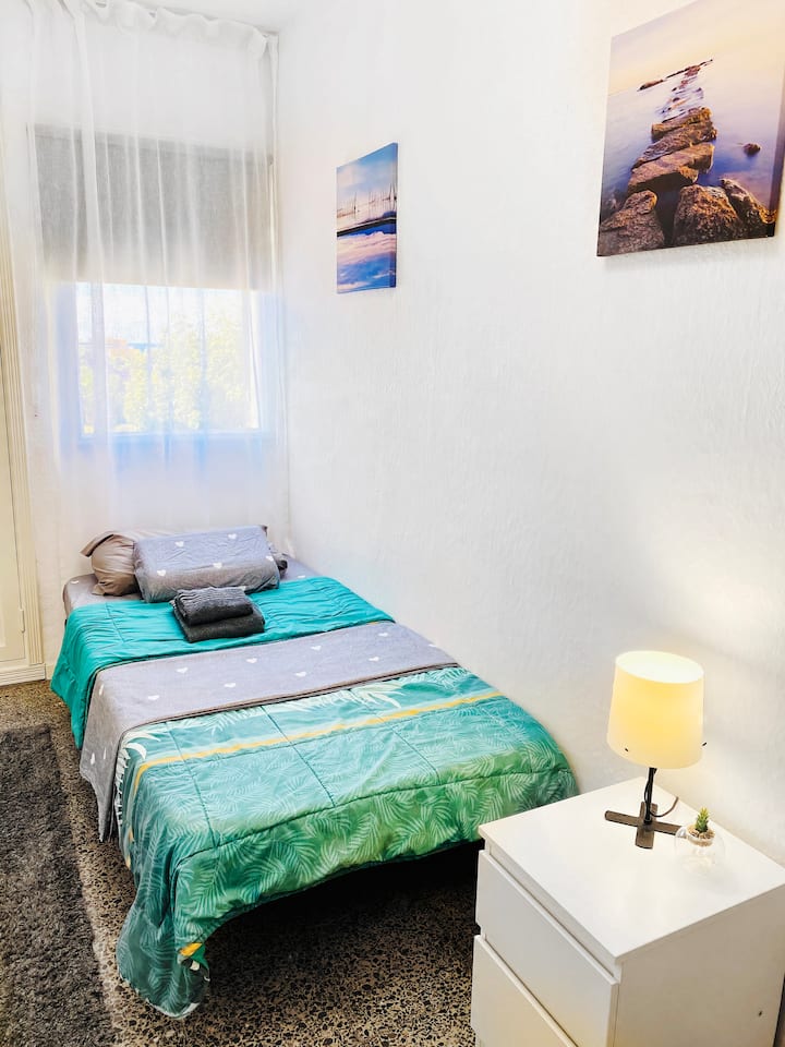 Kitanda cha mtu mmoja kilicho na meza na feni ya dari inayodhibitiwa kwa mbali na taa.