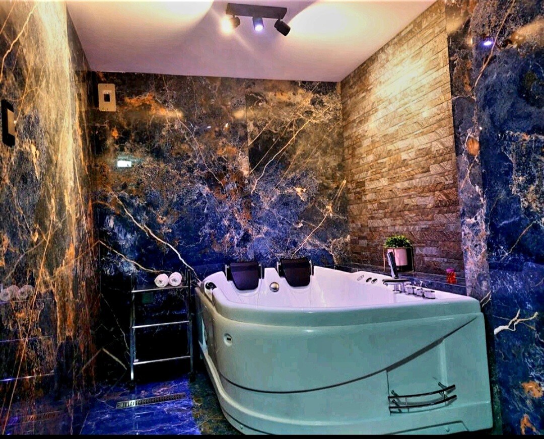 An elegantly designed bathroom features a large white jacuzzi surrounded by blue and gray marbled walls. Soft lighting highlights the textured surfaces, while neatly arranged towels are visible on a chrome rack nearby.